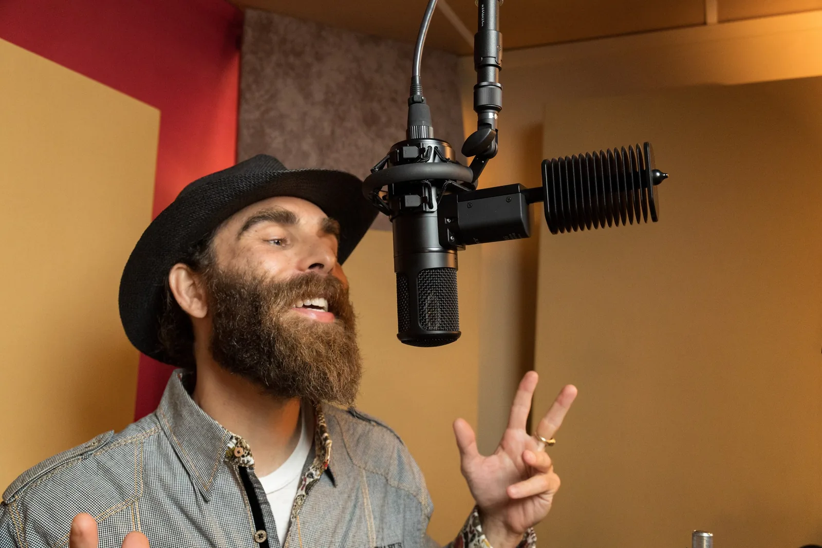 Photo: a vocalist tracking in the booth, singing into a large-diaphragm microphone on a shockmount with a pop filter